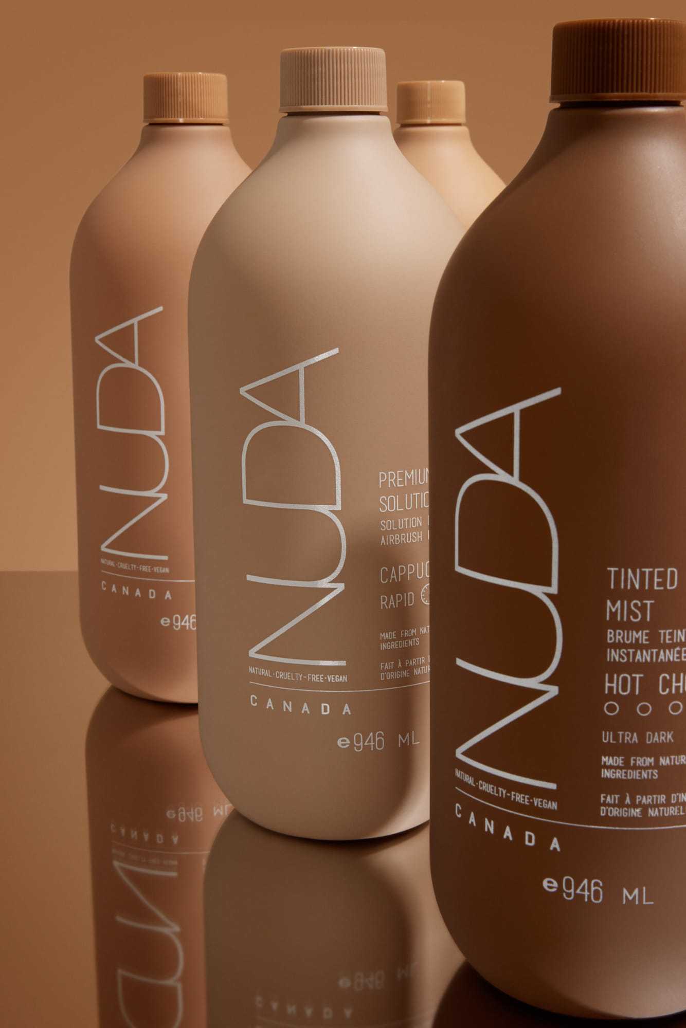 Bottles of NUDA tanning products in varying shades on a reflective surface.